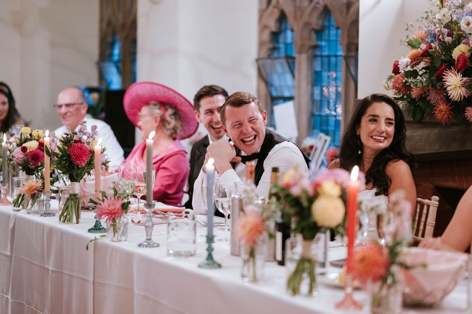 Wedding reception guests seated at elegant tables with pink floral centerpieces and candlelight in a historic venue.