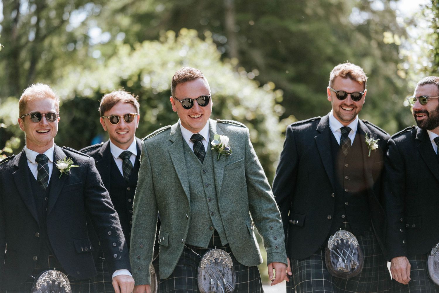 Aberdeen Wedding Photography. Groomsmen in traditional Scottish kilts and suits stand together outdoors at a wedding ceremony.