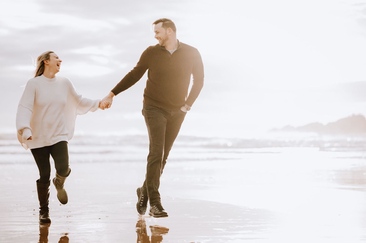 Engagement photography session Aberdeen. A couple runs playfully along a misty beach at sunset.