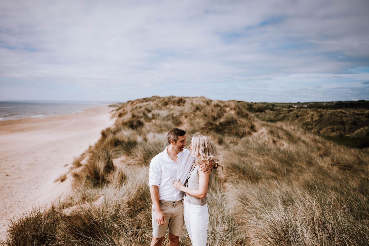Engagement photography session Aberdeen. A couple shares intimate moments among the coastal sand dunes under a cloudy sky.