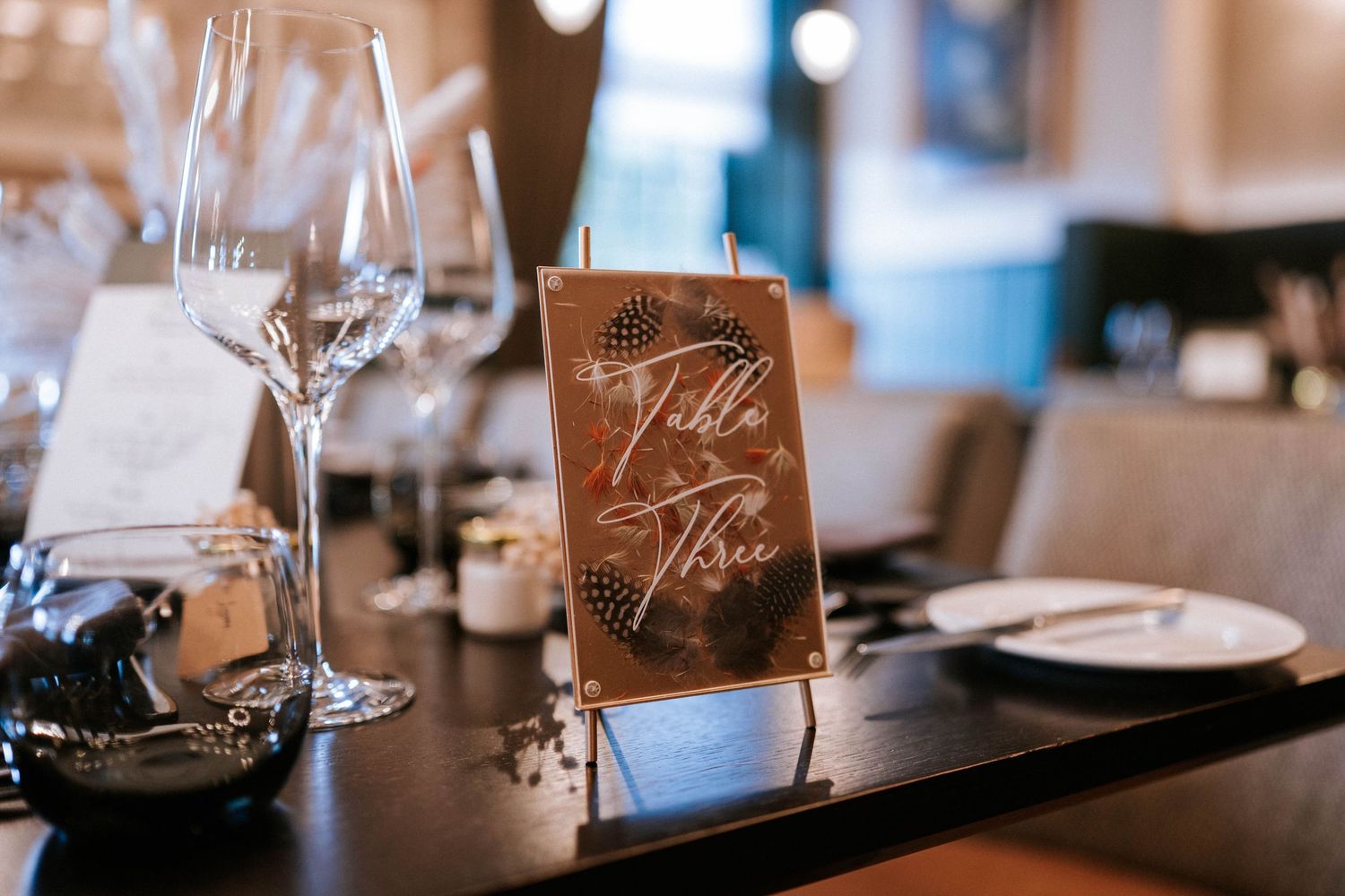 Wedding reception place settings with wooden name cards and wine glasses on elegant tables.