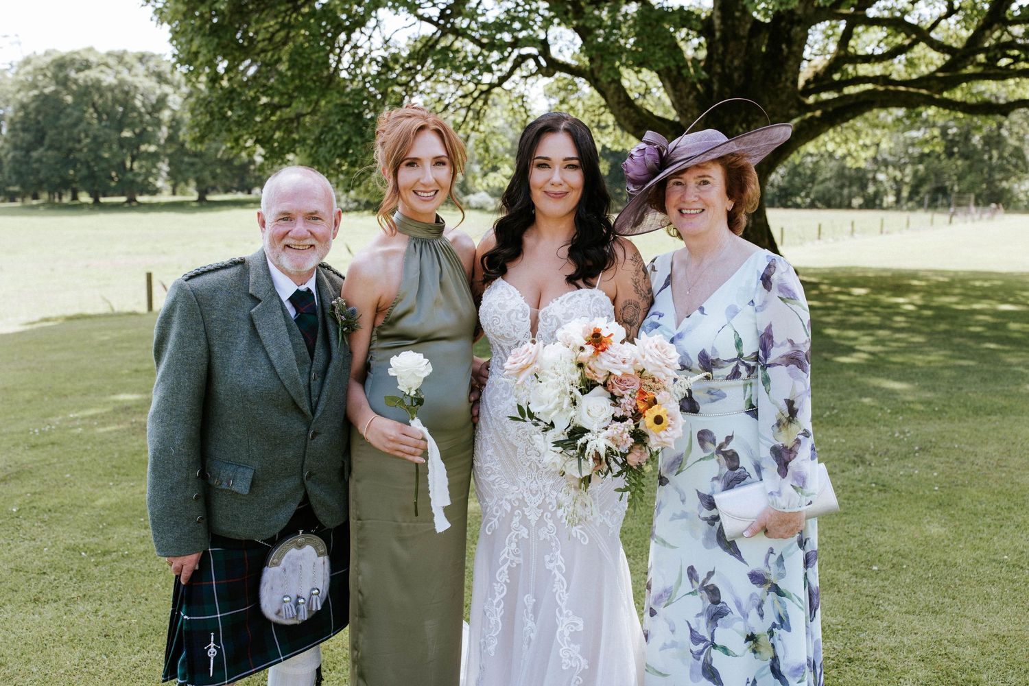 Wedding group portrait featuring traditional Scottish formal wear and sage green attire outdoors.