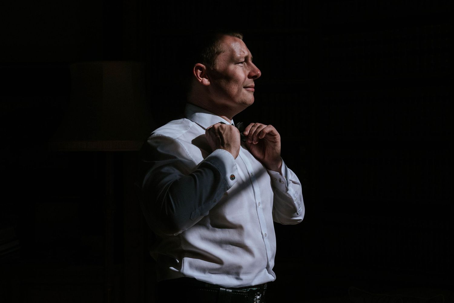 Silhouetted figure adjusting formal attire against dark background.