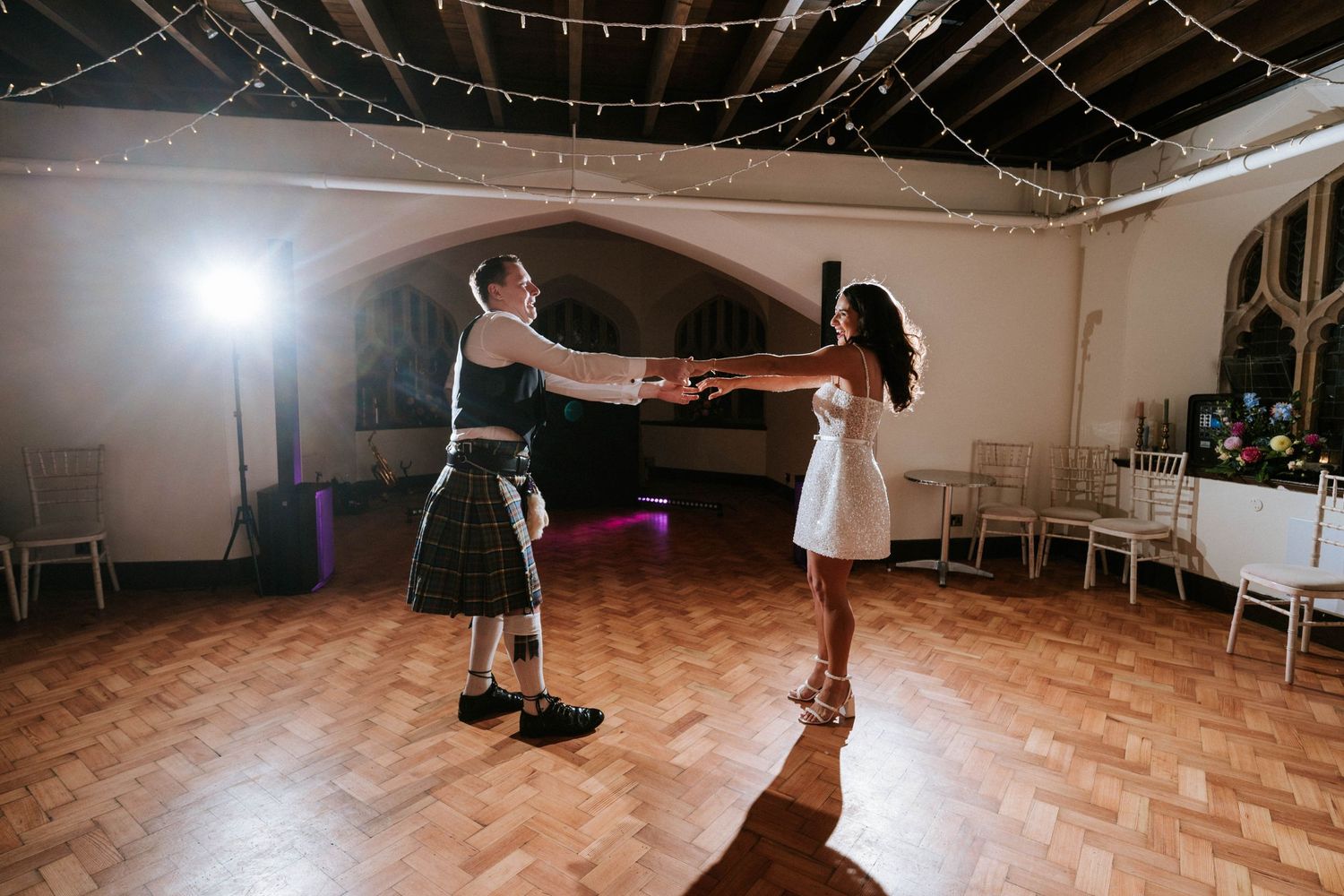 A couple dances together in a reception hall decorated with string lights.