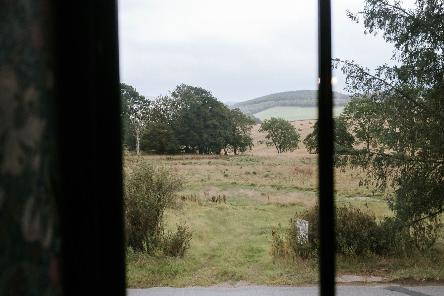 Rolling green hills and countryside landscape viewed through a dark window frame.