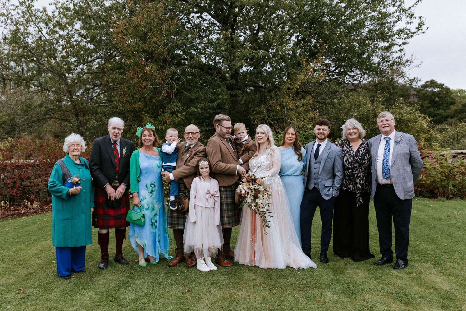 Wedding party and guests pose for group photos on a lush green lawn.