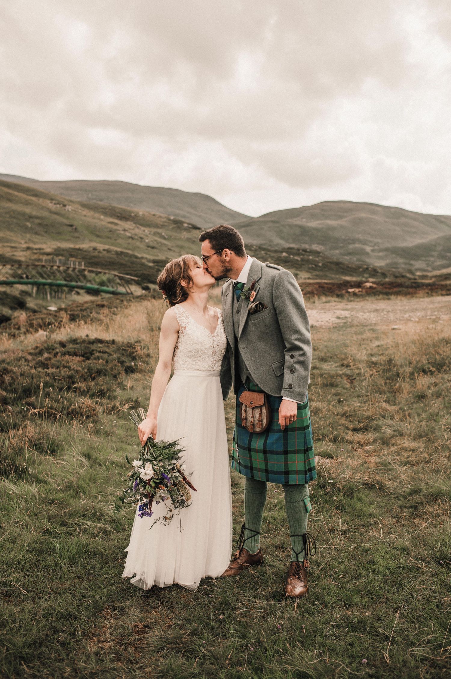 Romantic moment between newlyweds against dramatic Scottish Highland landscape.
