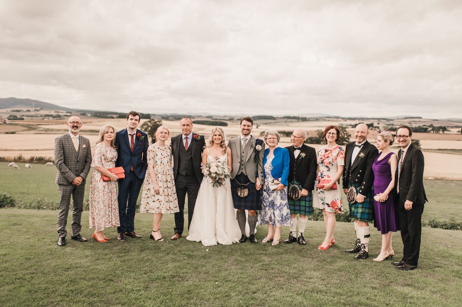 Extended family group photo at outdoor wedding with rolling hills in background.
