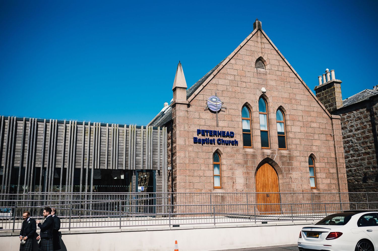 Modern architecture contrasts with traditional stone church building under bright blue sky.