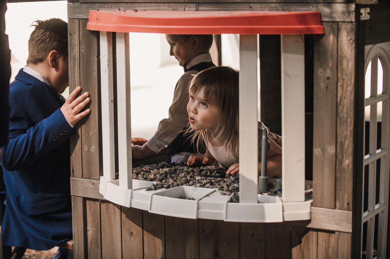 Children play in a wooden playhouse while an adult watches from outside.