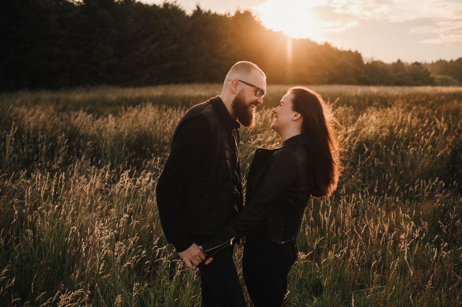 Intimate couple sharing tender moment in field during golden hour sunset.
