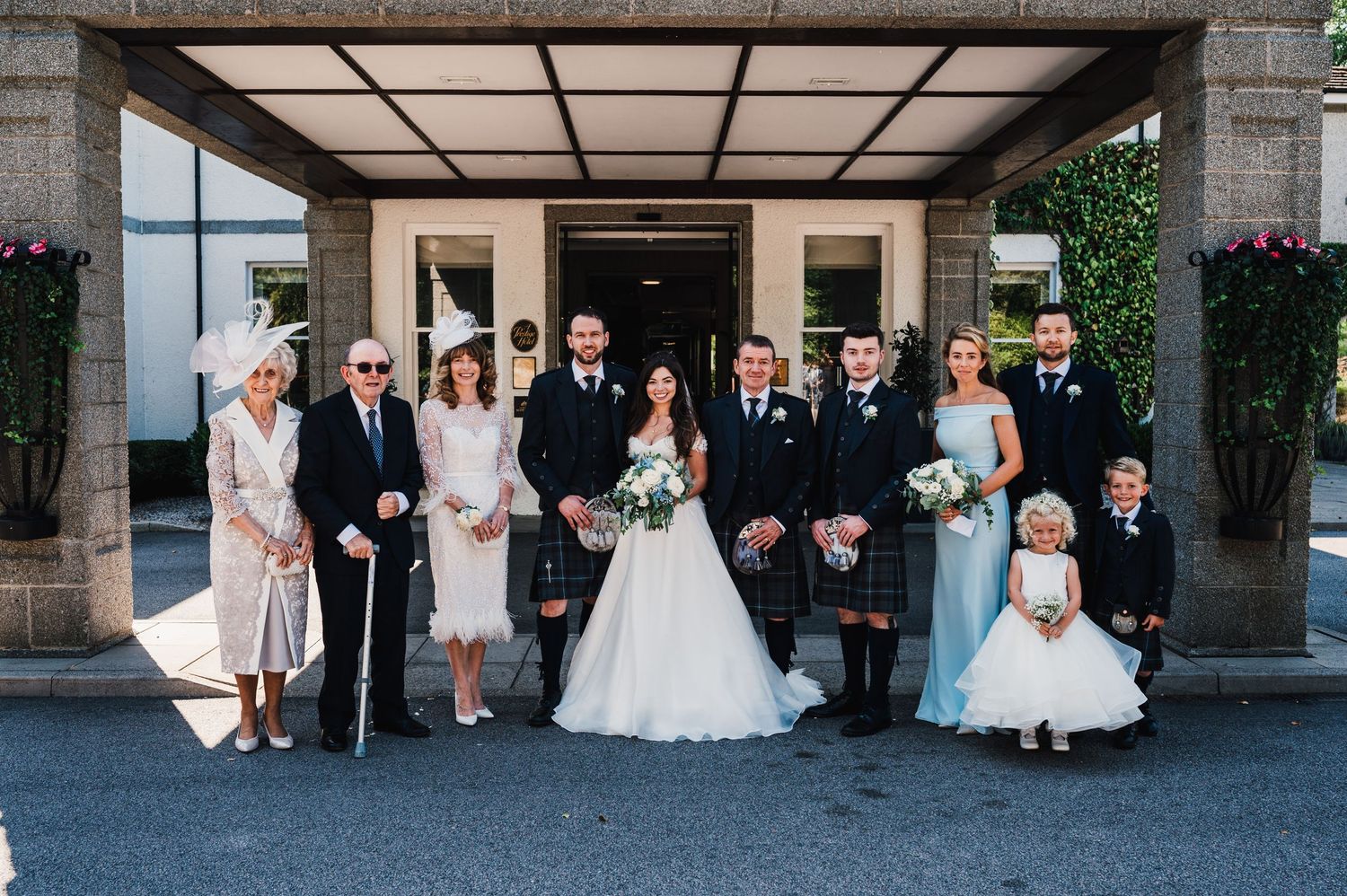 Large wedding party group photo showing mix of formal attire and traditional Scottish kilts.