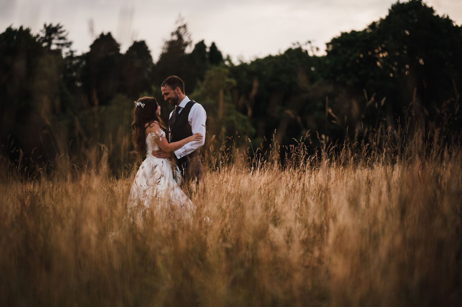 A couple shares an intimate moment in tall grass during golden hour.