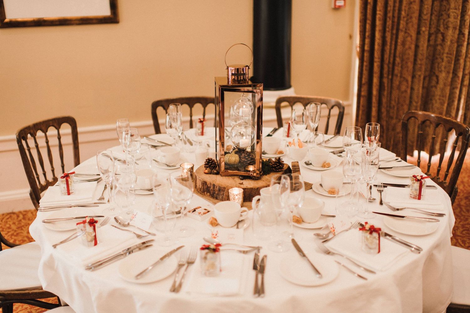 A formal table setting with white linens, elegant place settings and a centerpiece with lanterns.