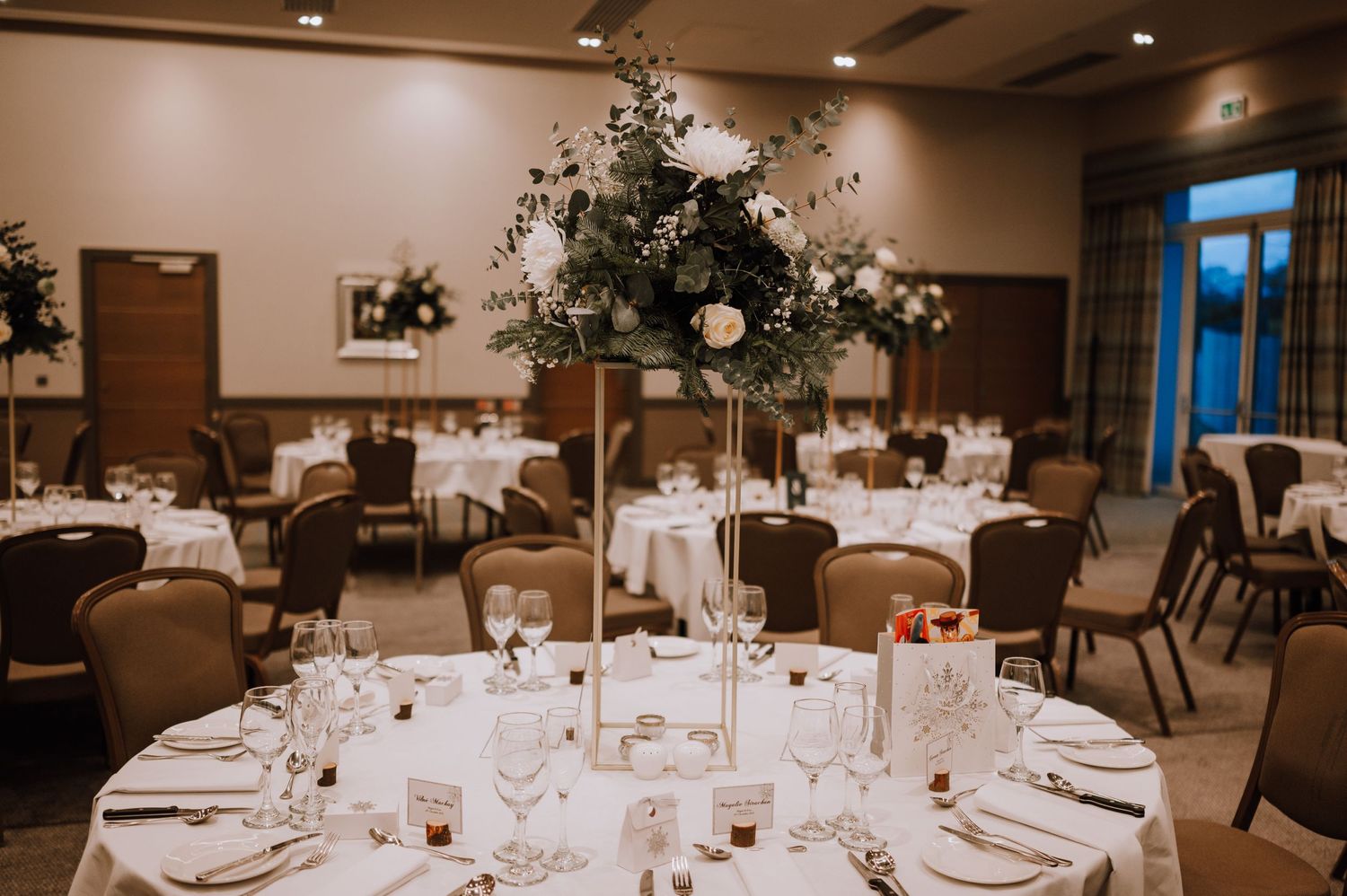 Formal wedding reception tables set with white linens and tall floral centerpieces.