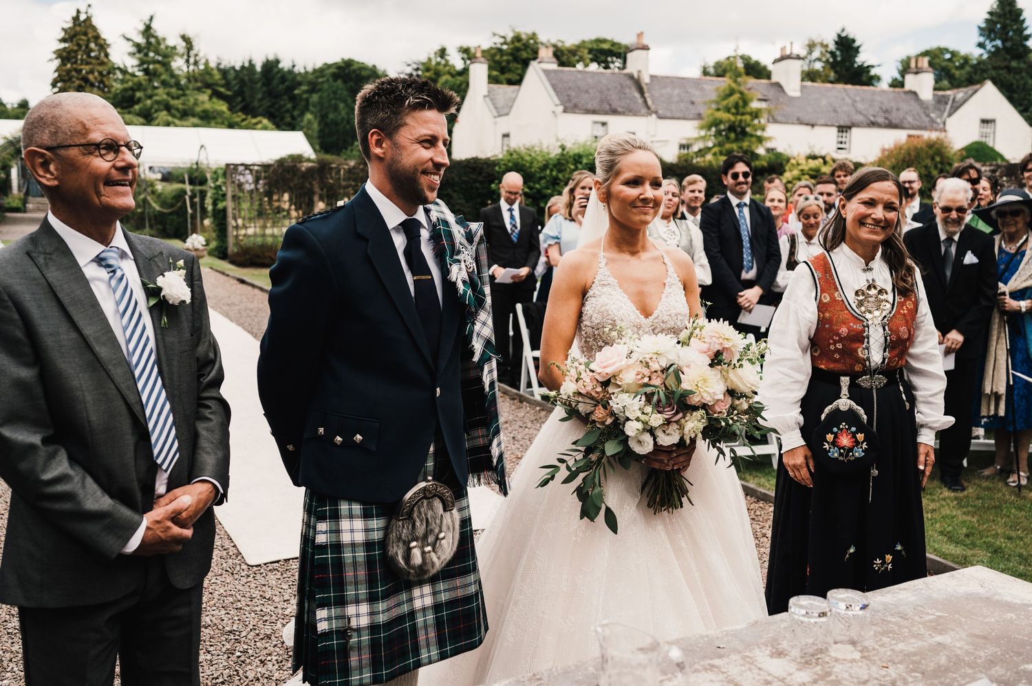 Scottish wedding celebration with kilts and traditional attire in garden setting.