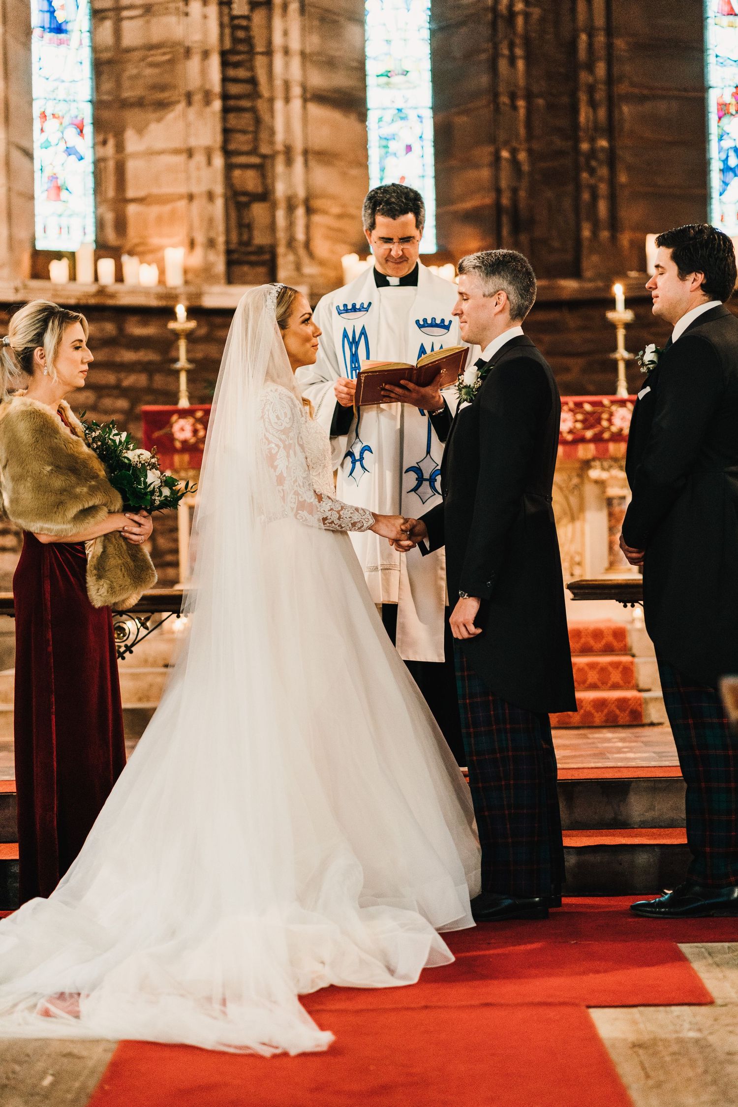 A wedding ceremony in progress at an ornate church with stained glass windows and red carpet.