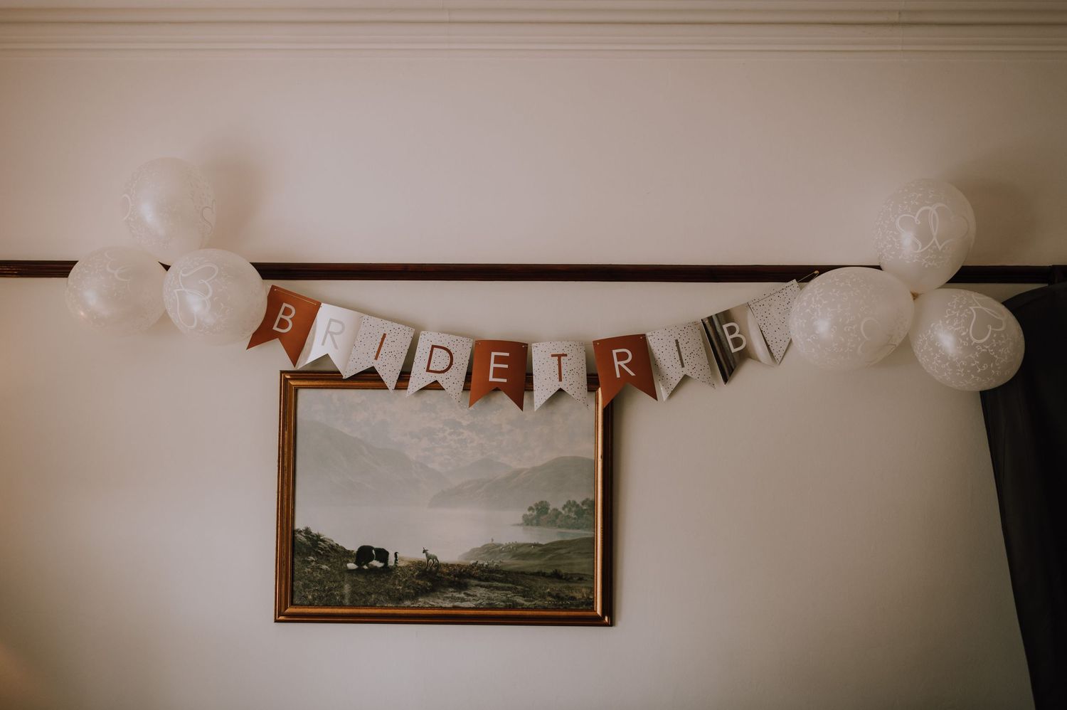 Wedding decorations feature a rustic 'Here' banner and white balloons hanging above a landscape painting.