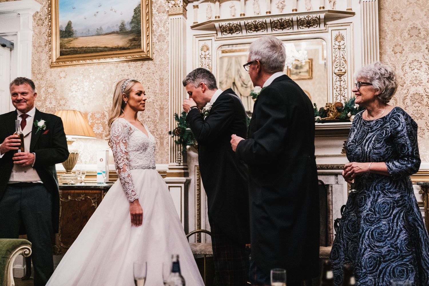 A wedding ceremony takes place in an elegant room with ornate moldings and landscape paintings.