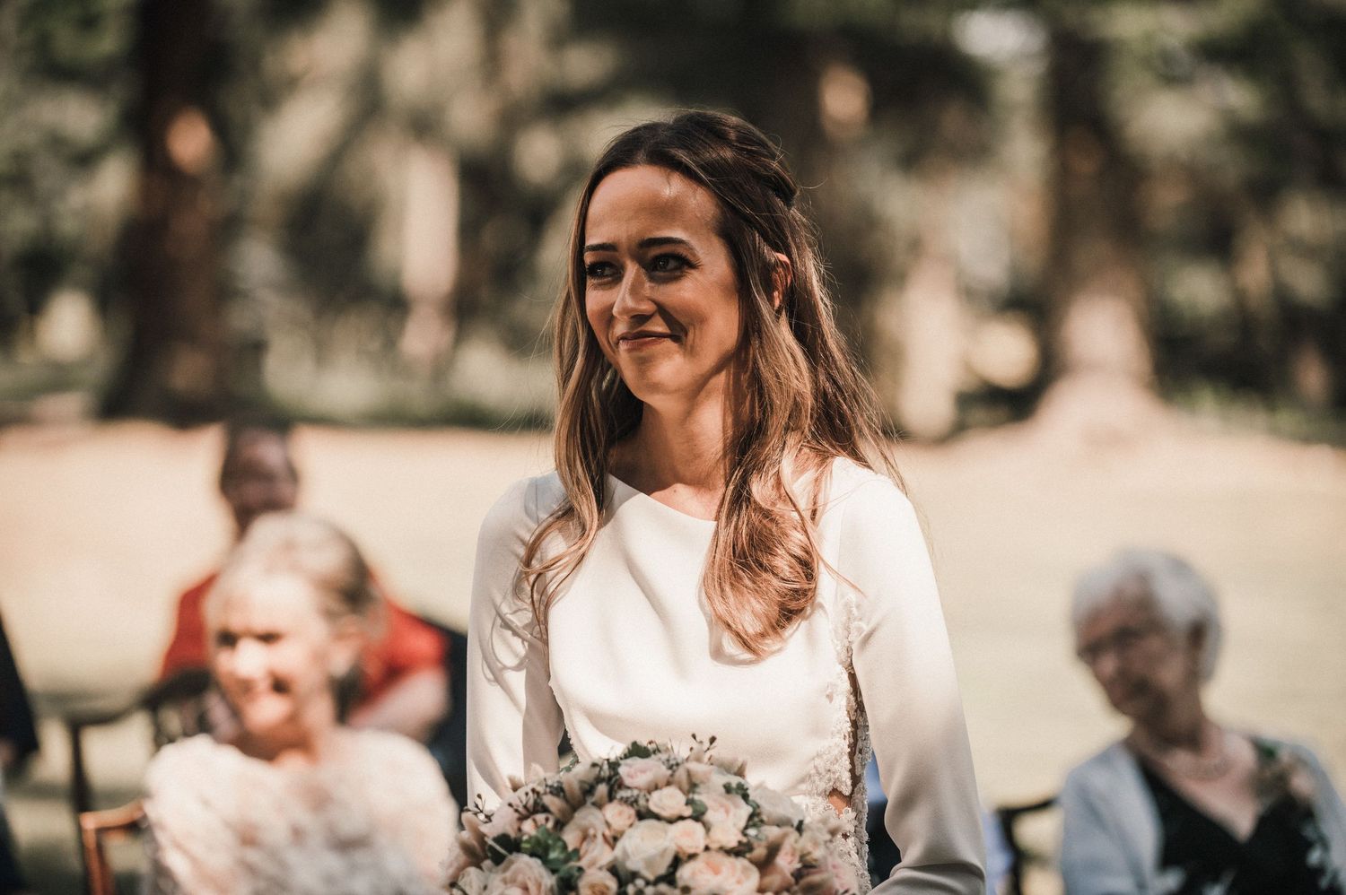 A joyful bride holds her bouquet during an outdoor forest wedding ceremony.