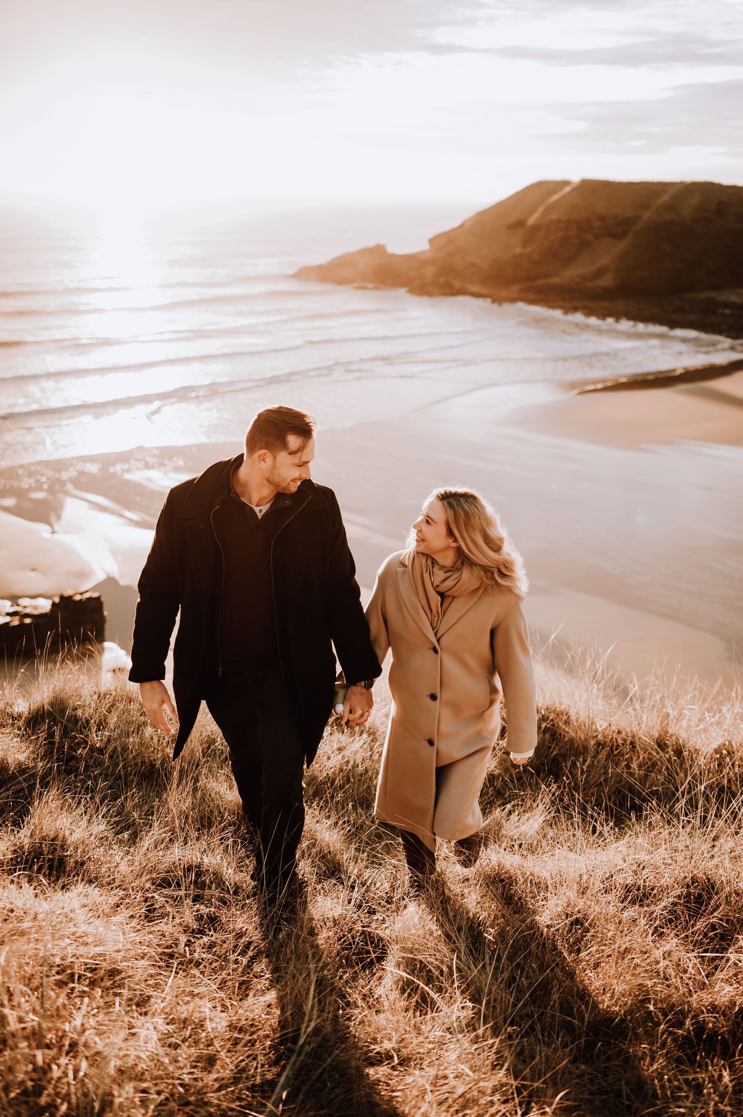 Couple hiking together along scenic coastal path during golden hour.