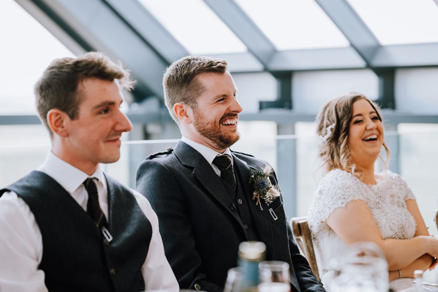 Wedding party members laugh together during speeches at an elegant reception.