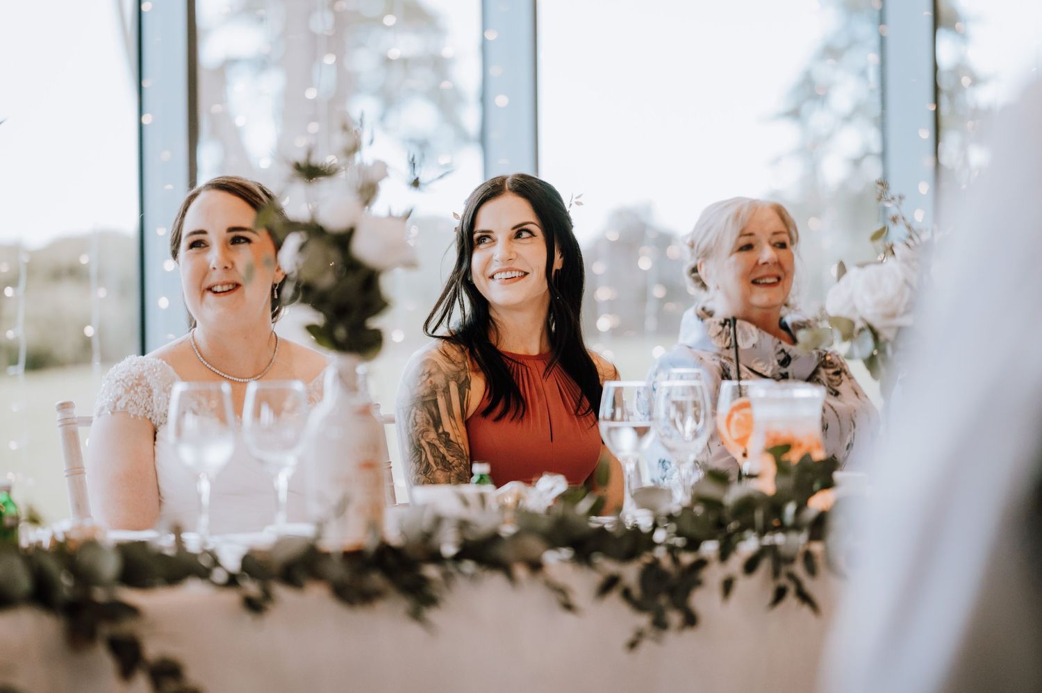 Wedding reception guests enjoying speeches at head table with floral decorations.