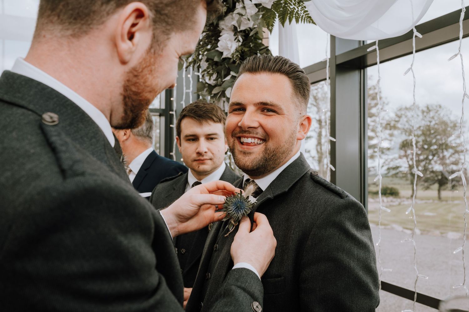 Groomsmen help adjust a tie before a Scottish wedding ceremony.
