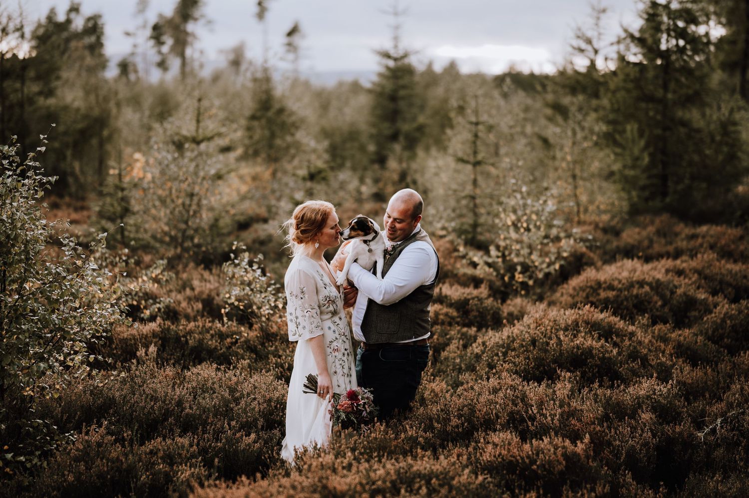 A couple shares an emotional moment in a heather field surrounded by forest.