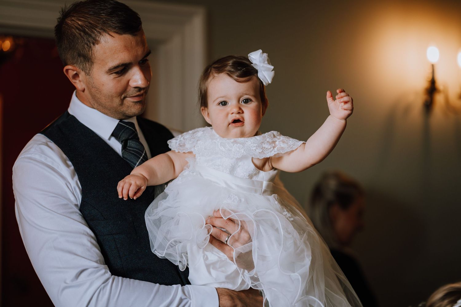 Baby in white christening gown held up during special celebration.
