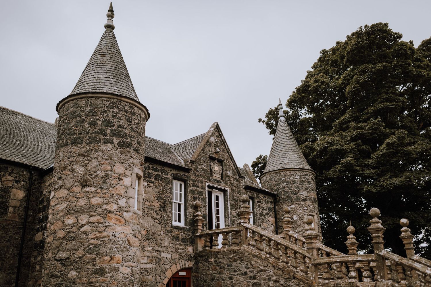 Gothic stone castle with turrets and traditional Scottish architecture against cloudy sky.