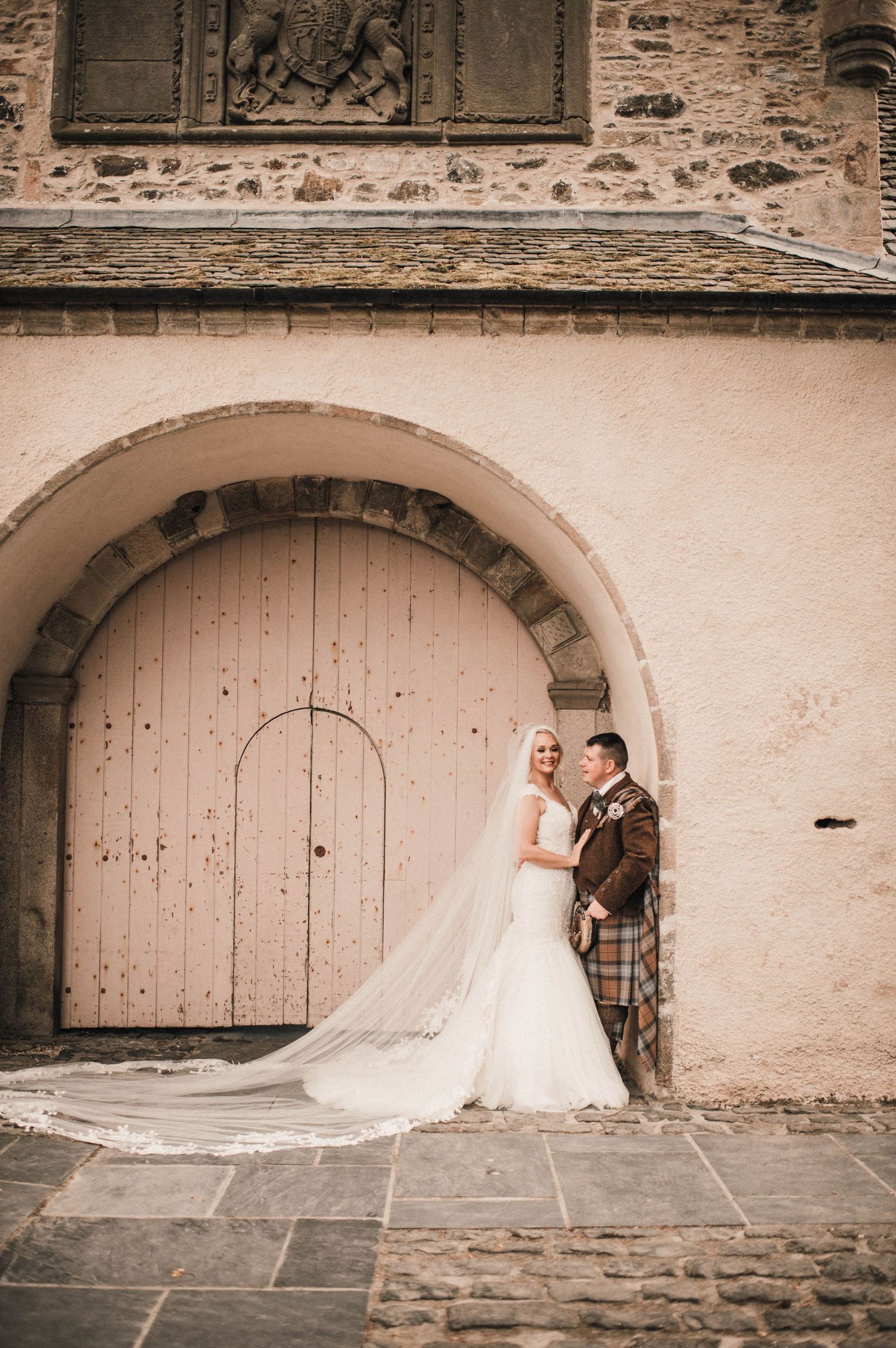 A romantic wedding portrait under a stone archway with vintage architectural details.