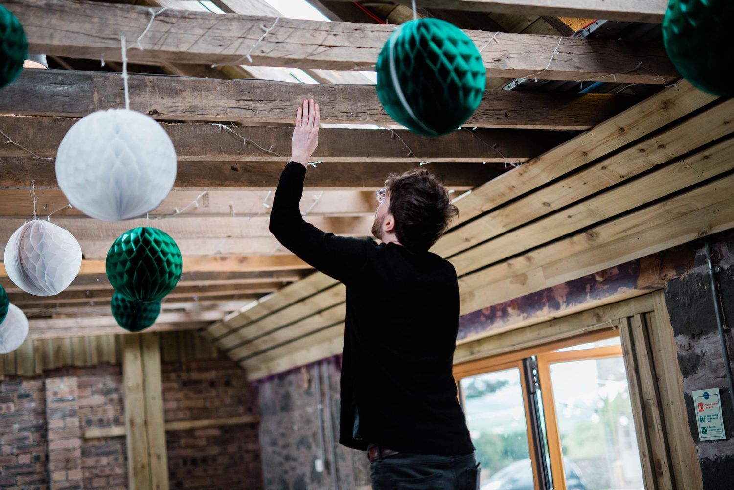 Silhouette of person hanging decorations from wooden beam ceiling with paper lanterns.