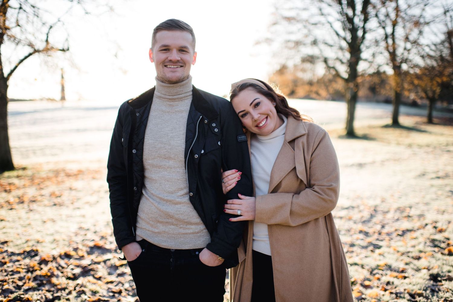 Happy couple posing outdoors on crisp autumn day with golden sunlight.