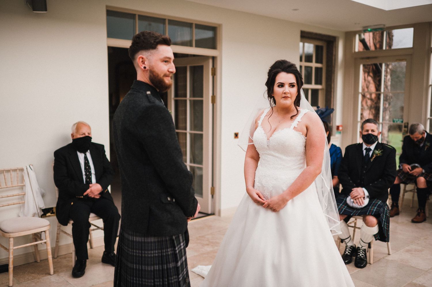 A couple exchanges vows during an intimate indoor wedding ceremony with Scottish formal attire.