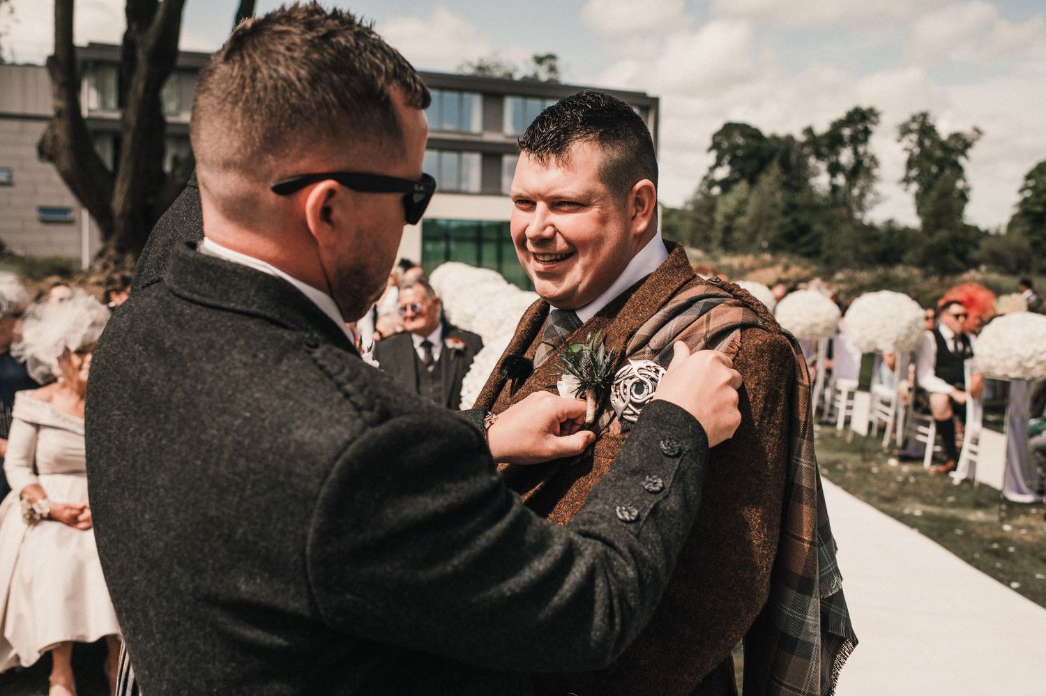 Two groomsmen in traditional Scottish attire share a lighthearted moment before the ceremony.