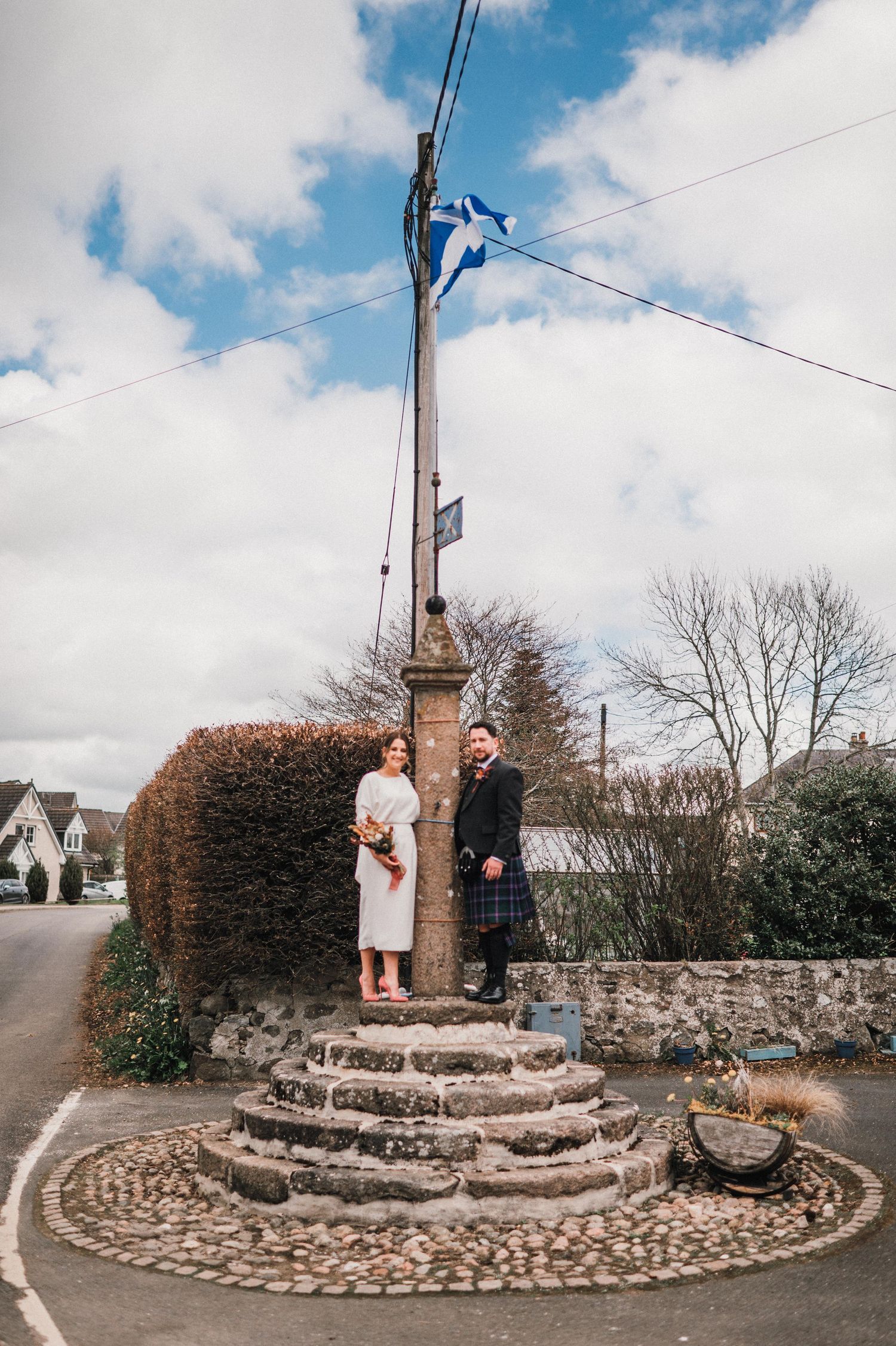 Wedding couple standing at historic stone monument with Scottish flag flying overhead.