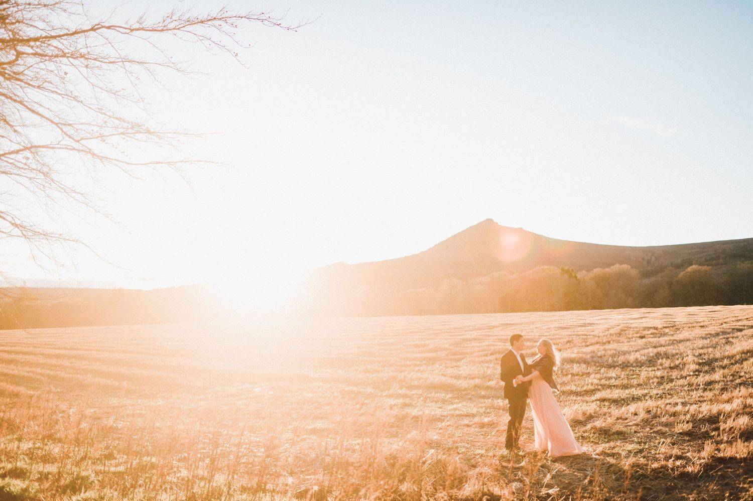 Silhouettes of a couple standing in a golden field with sunburst and mountain backdrop.