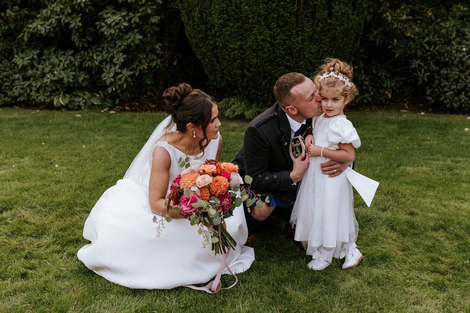 Intimate wedding moments captured on a sunny lawn with formal attire and Scottish traditional dress.