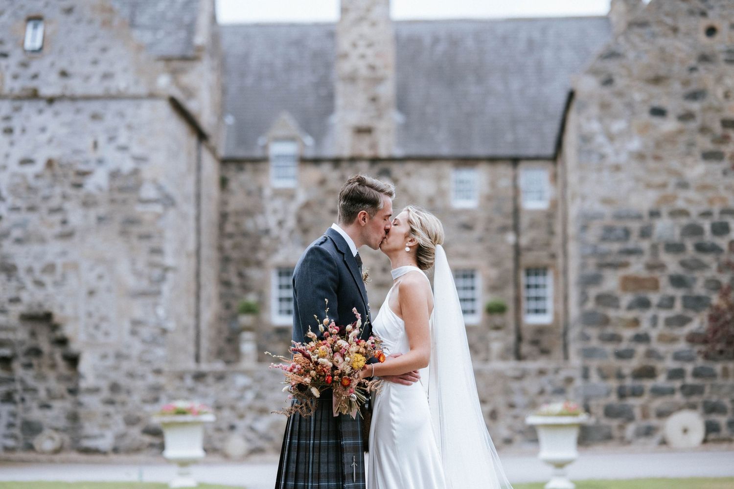 A couple shares an intimate moment in front of a historic stone church building.