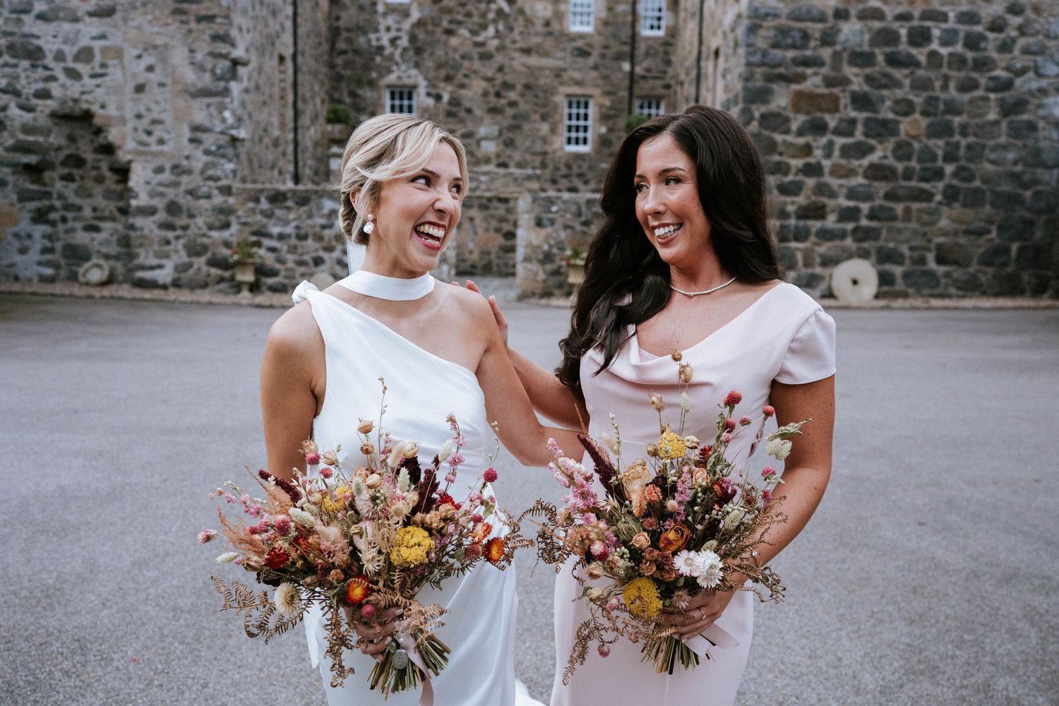 Wedding party members holding autumn-colored bouquets against stone wall backdrop.