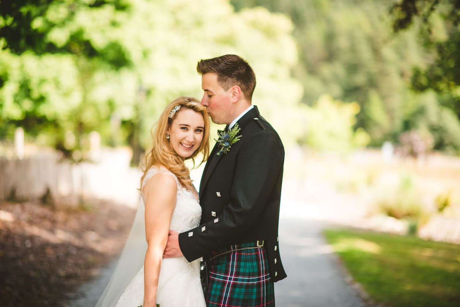 Couple poses together on a tree-lined path during a wedding photoshoot.