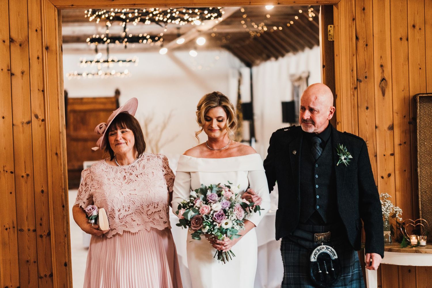 Wedding reception setup in rustic wooden barn with string lights and pink floral decorations.