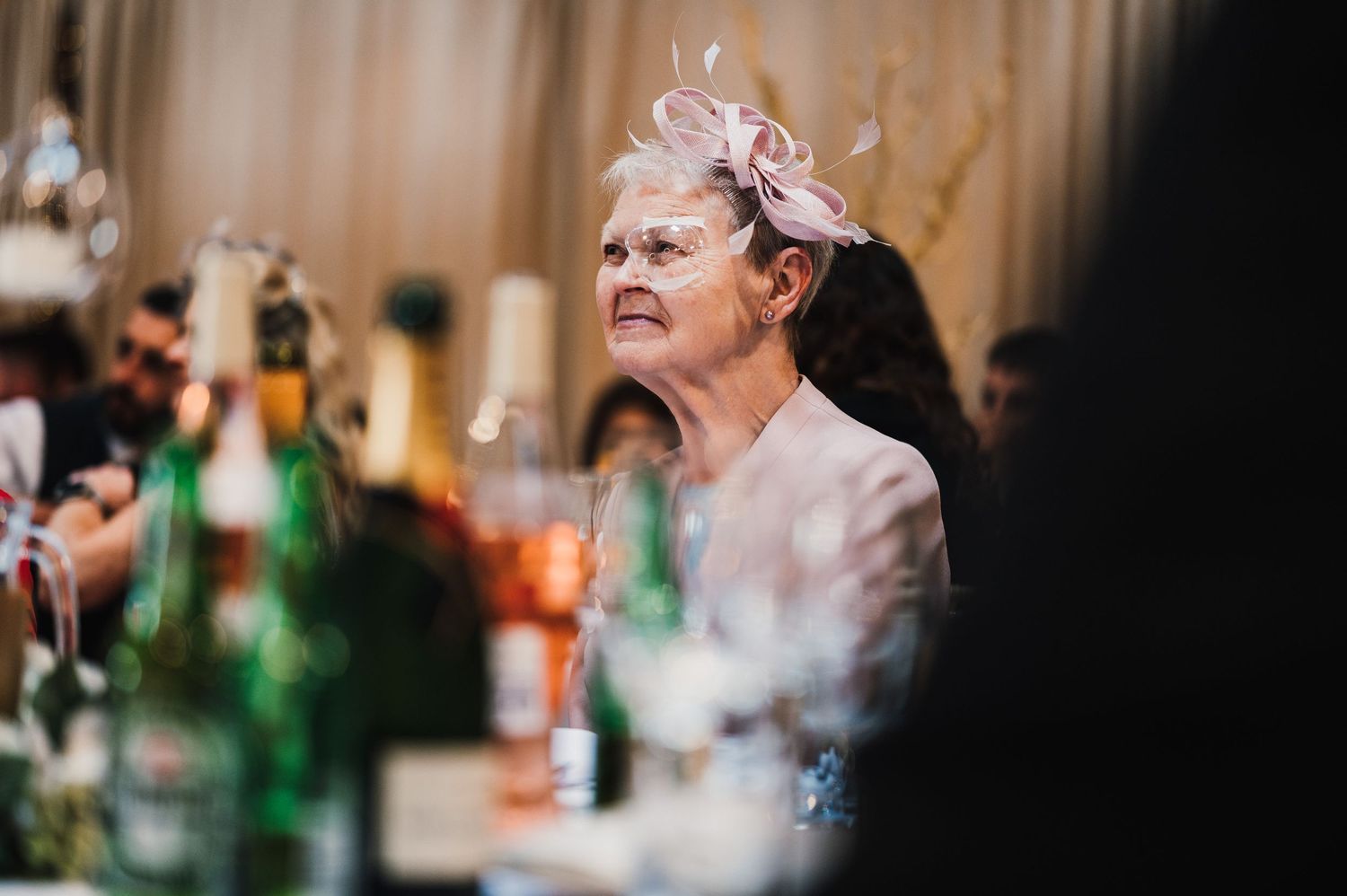 A dimly lit wedding reception scene with soft focus on glassware and decorative elements.