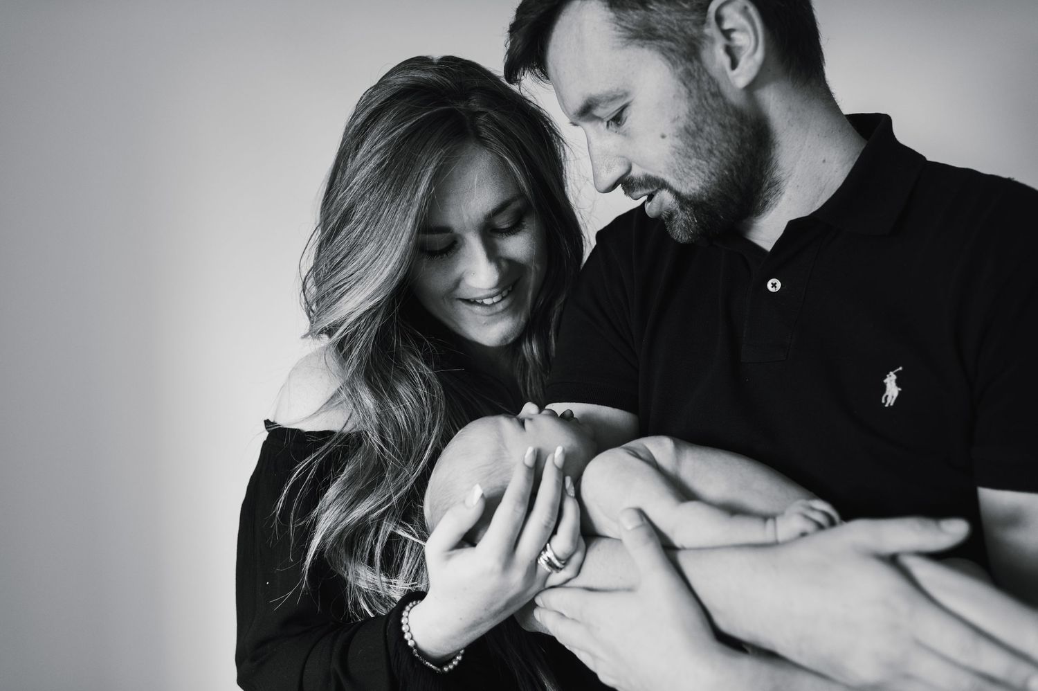 Black and white portrait of parents lovingly gazing at their newborn baby in their arms.