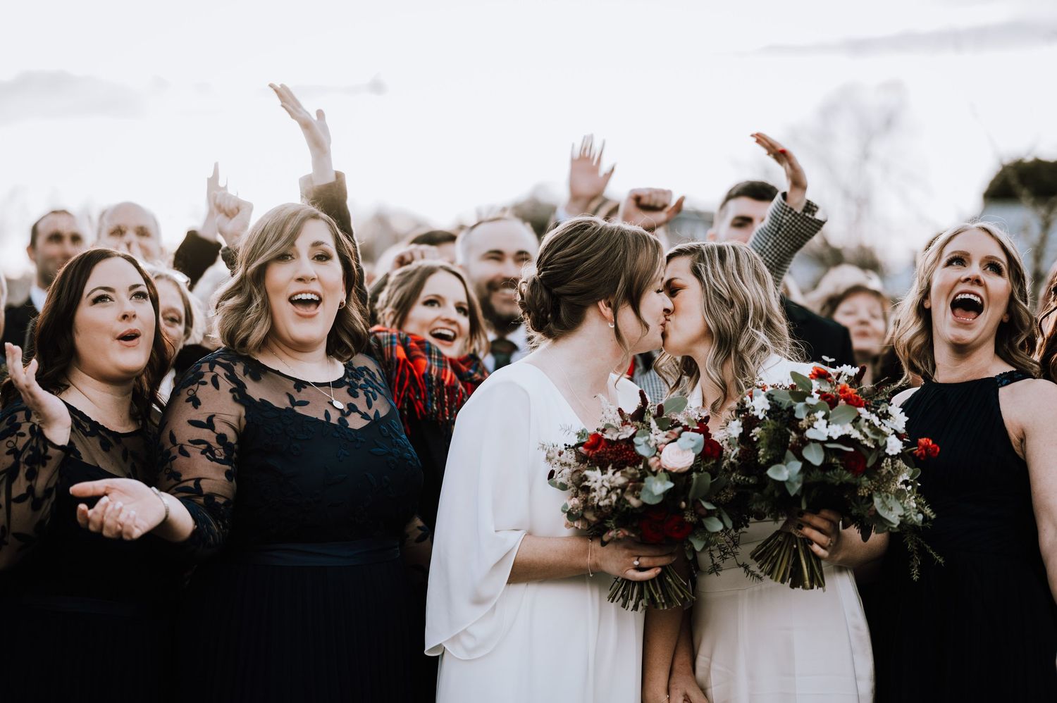 Same Sex Wedding Photography. Wedding celebration with cheering guests and burgundy bouquets against winter backdrop.