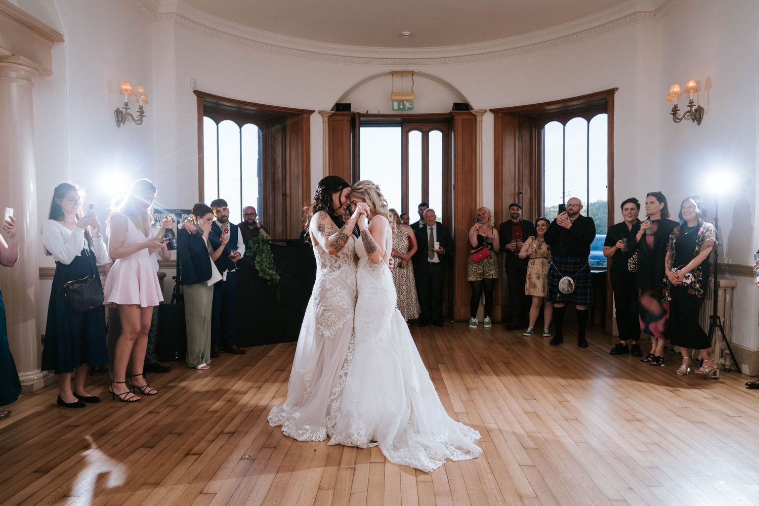 Fasque Castle Wedding Photography. Wedding guests gather in an elegant ballroom with white walls and wooden floors for a celebration.
