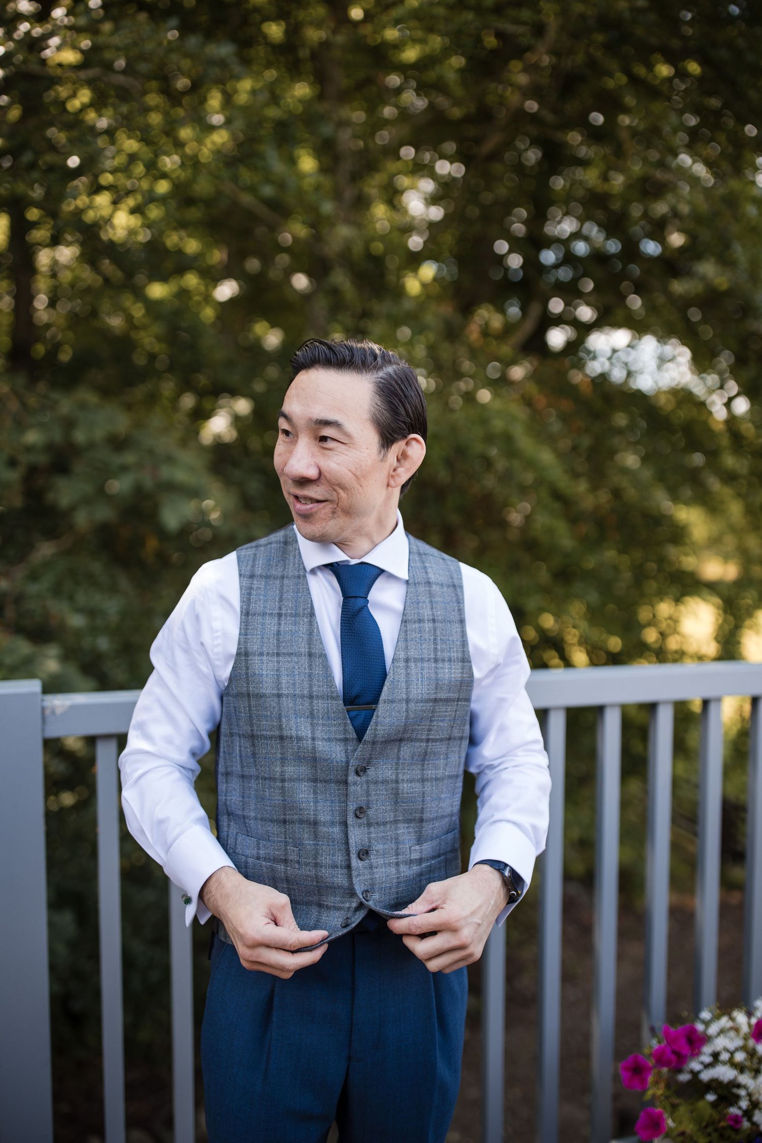 Person wearing gray vest and blue tie poses outdoors near white railing.
