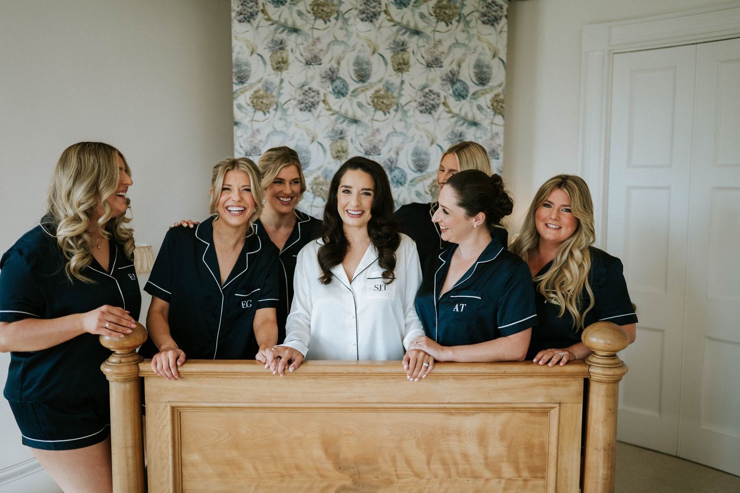 Wedding party members lean against a wooden banister in matching navy robes.