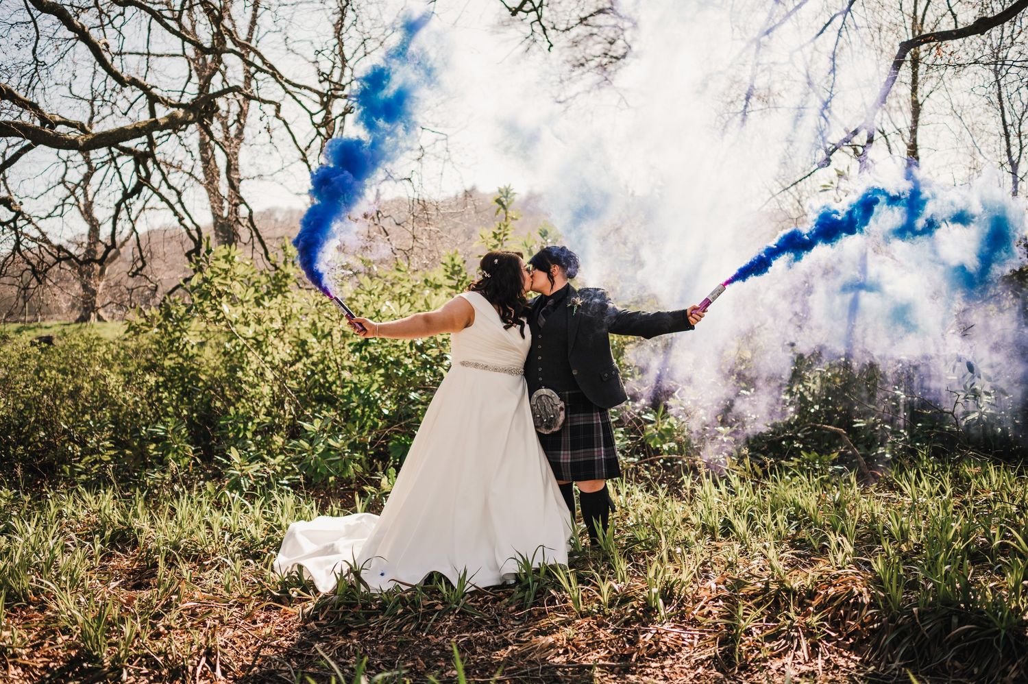 Logie House Wedding Photography. Wedding couple creates a dramatic scene with blue and white smoke bombs in a natural outdoor setting.